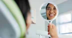 A woman is looking at her reflection in a hand mirror.