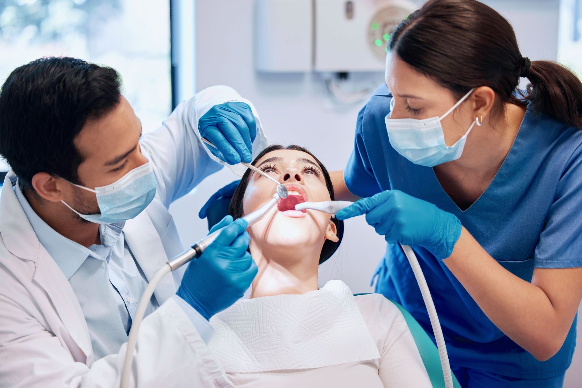 A woman is getting her teeth examined by two dentists in a dental office.