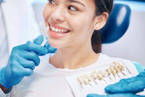 A woman is smiling while sitting in a dental chair while a dentist examines her teeth.