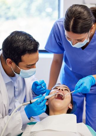 A dentist and a nurse are examining a patient 's teeth in a dental office.