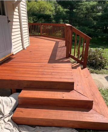 Wooden deck with a short set of steps and railing beside a house, overlooking a green yard