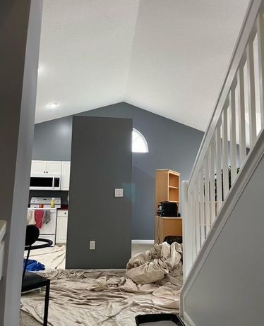 Living room under renovation with plastic-covered floor, gray accent wall, staircase, and exposed shelving.