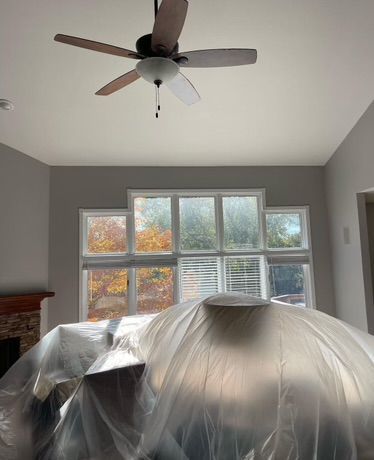 A living room with a ceiling fan and a vase covered in plastic.
