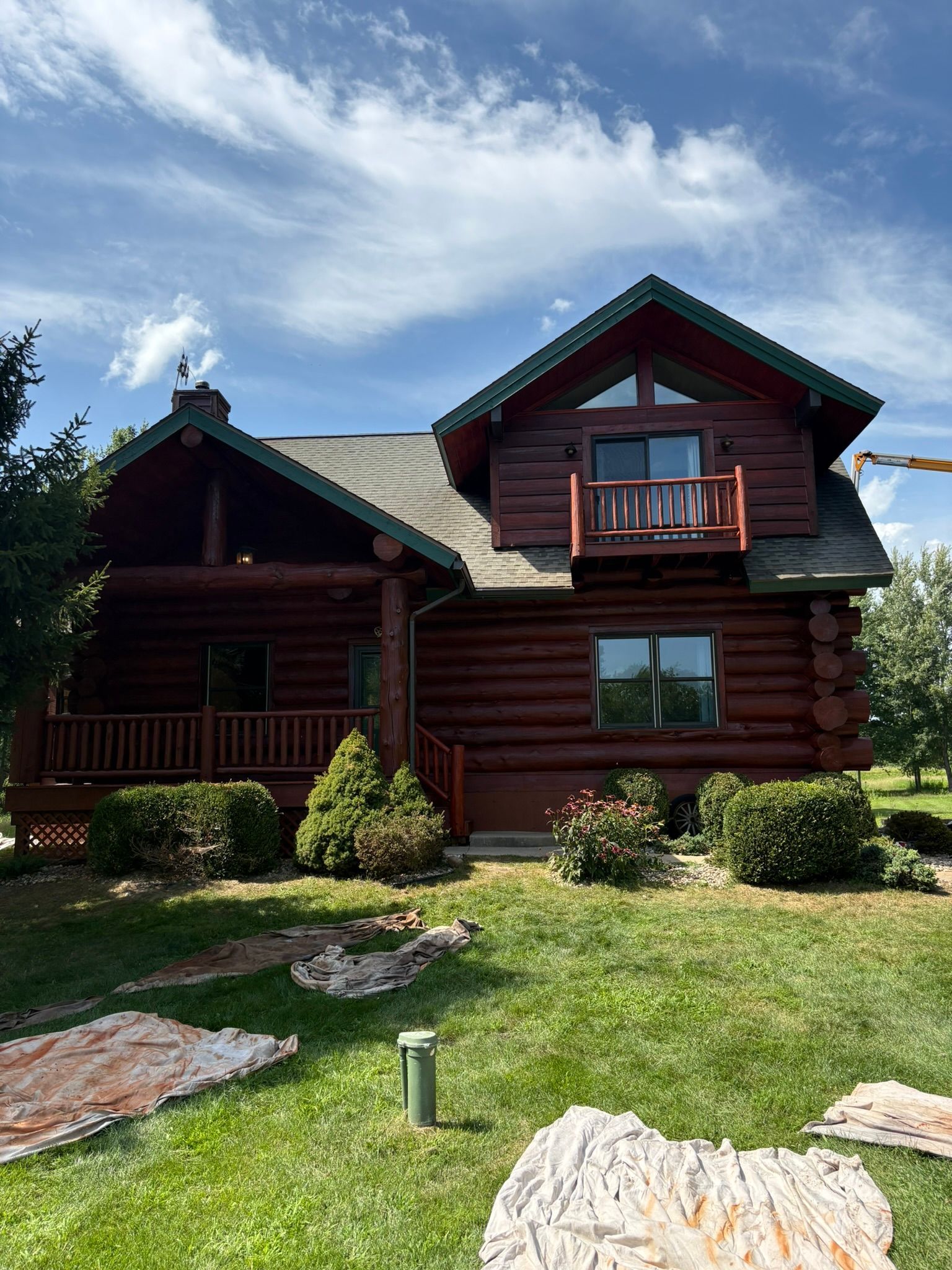Log cabin house with green roof and small balcony, surrounded by lawn and rocks under a blue sky