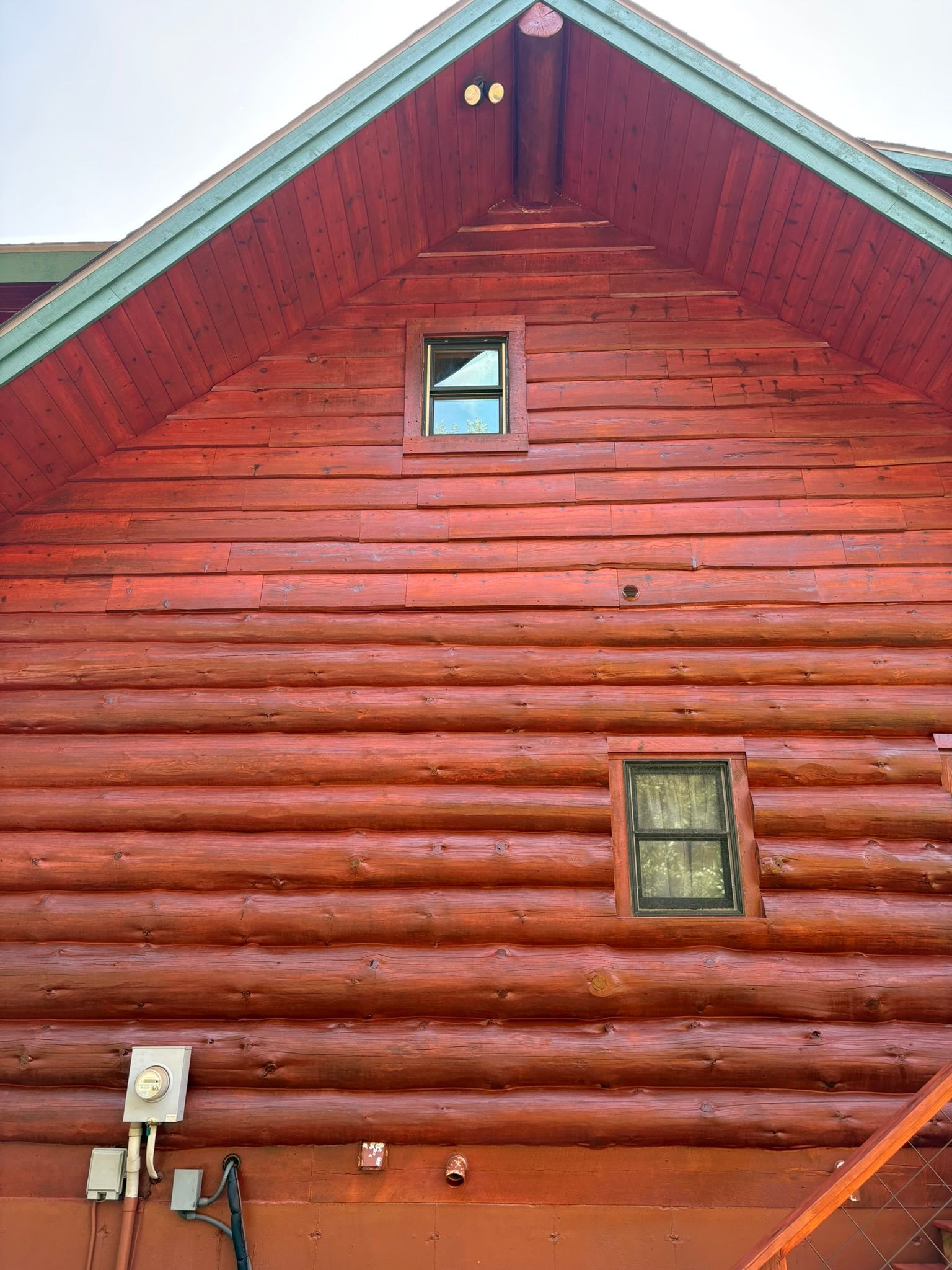 Red wooden cabin exterior with two small windows and a green-trimmed roofline
