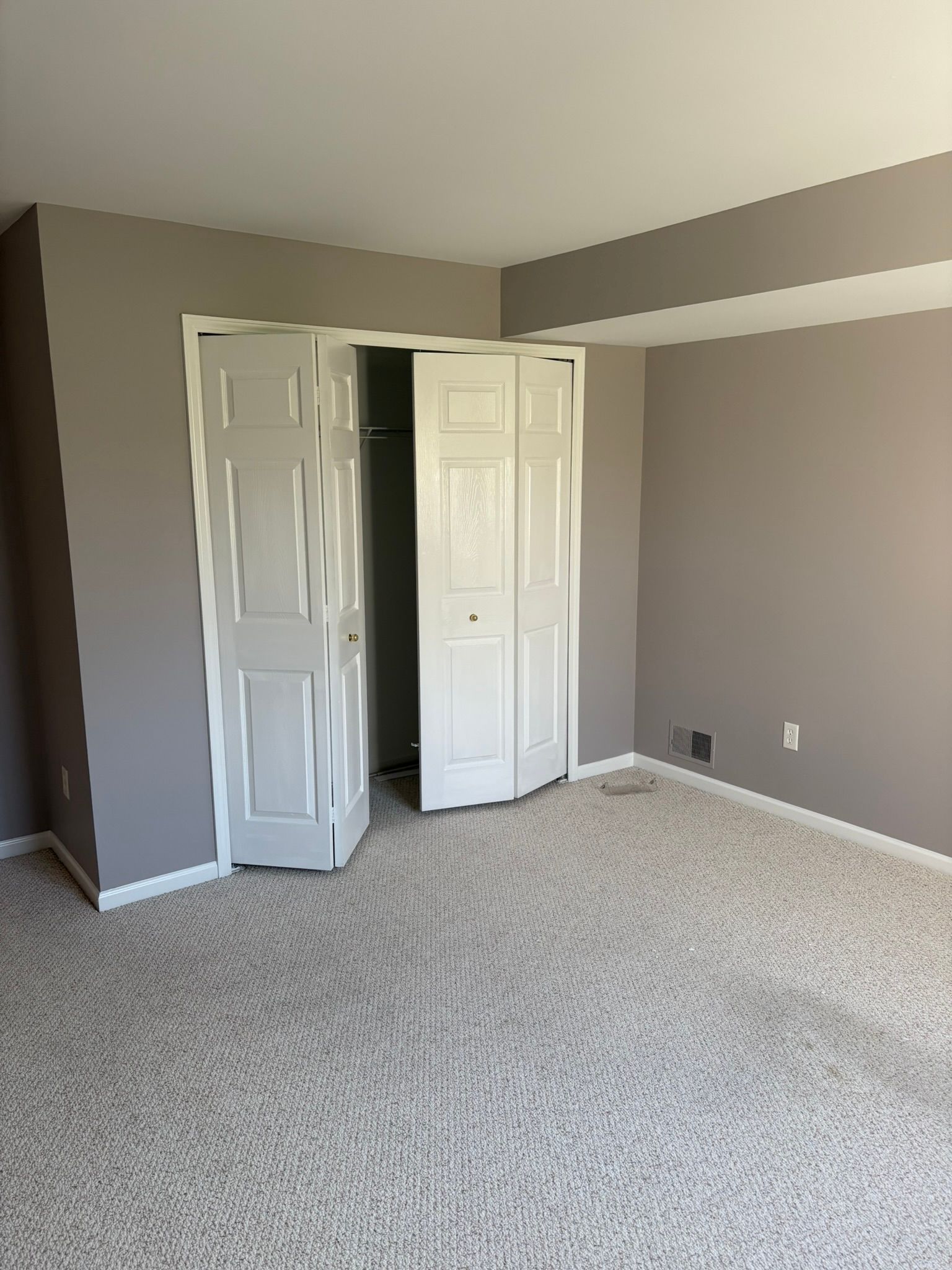 Empty beige bedroom with open white closet doors and carpeted floor