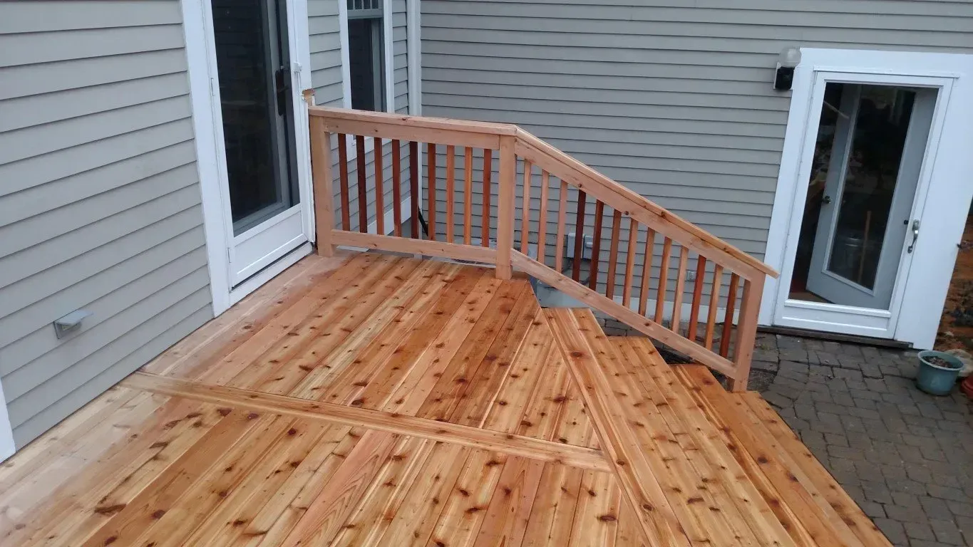 Wooden deck with stairs, railing, and doors to a house.