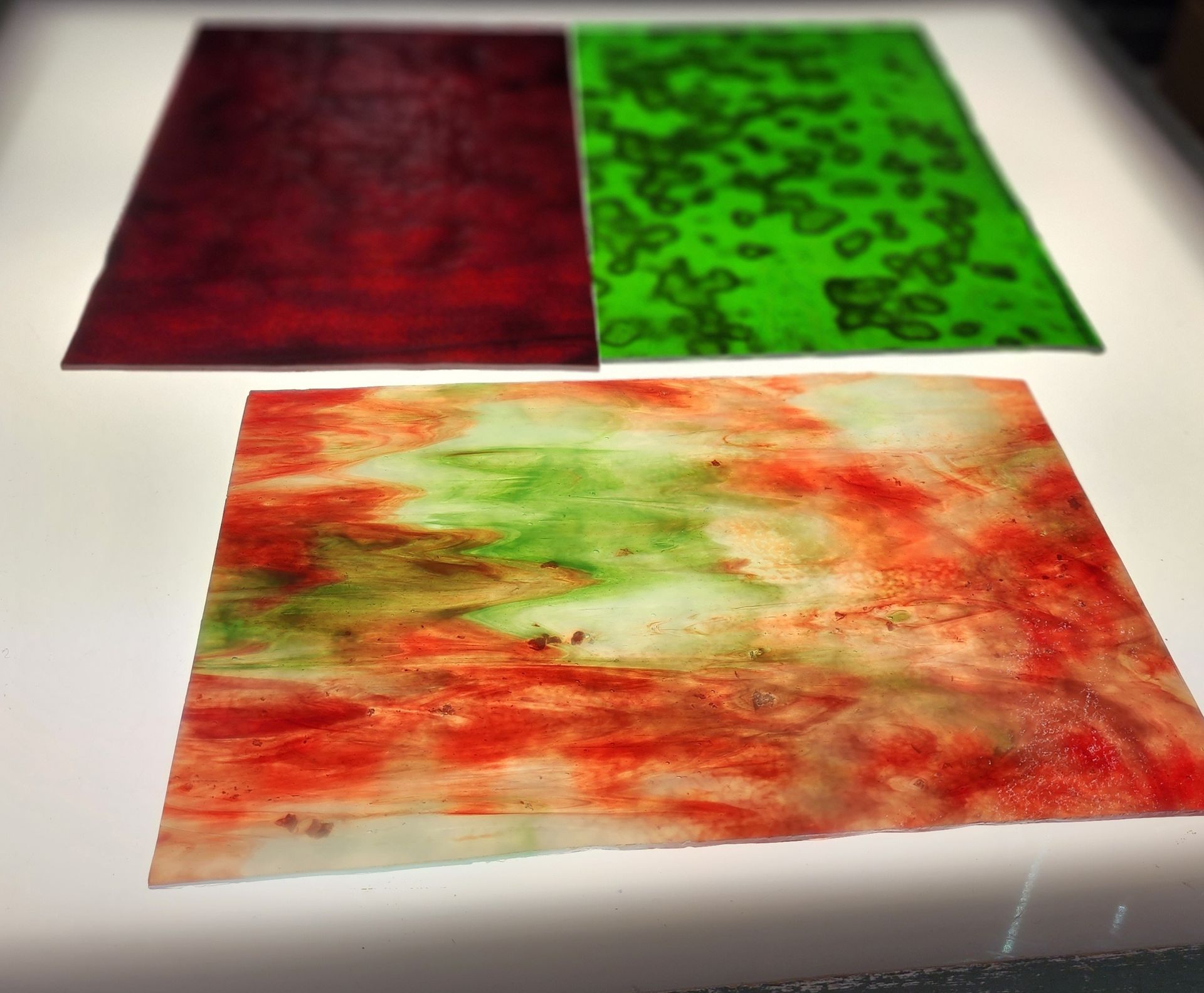 Deep burgundy red and green mottled Chicago Art Glass in background with bright orange and green art glass in foreground. 