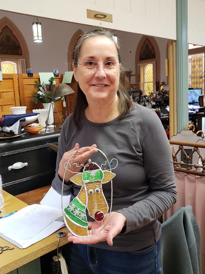 Stained Glass Workshop student showing her completed  project festuring a reindeer in an oval with Christmas decorations. 