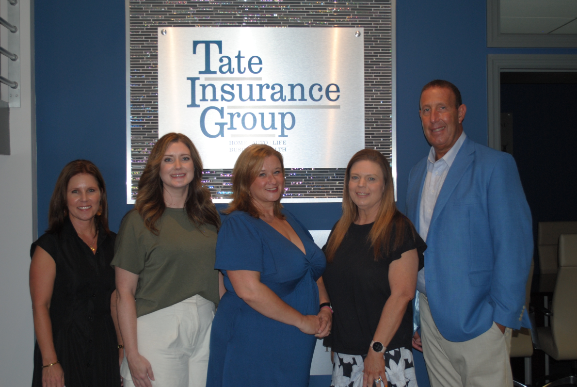 Five people posing in front of a Tate Insurance Group sign in an office lobby.