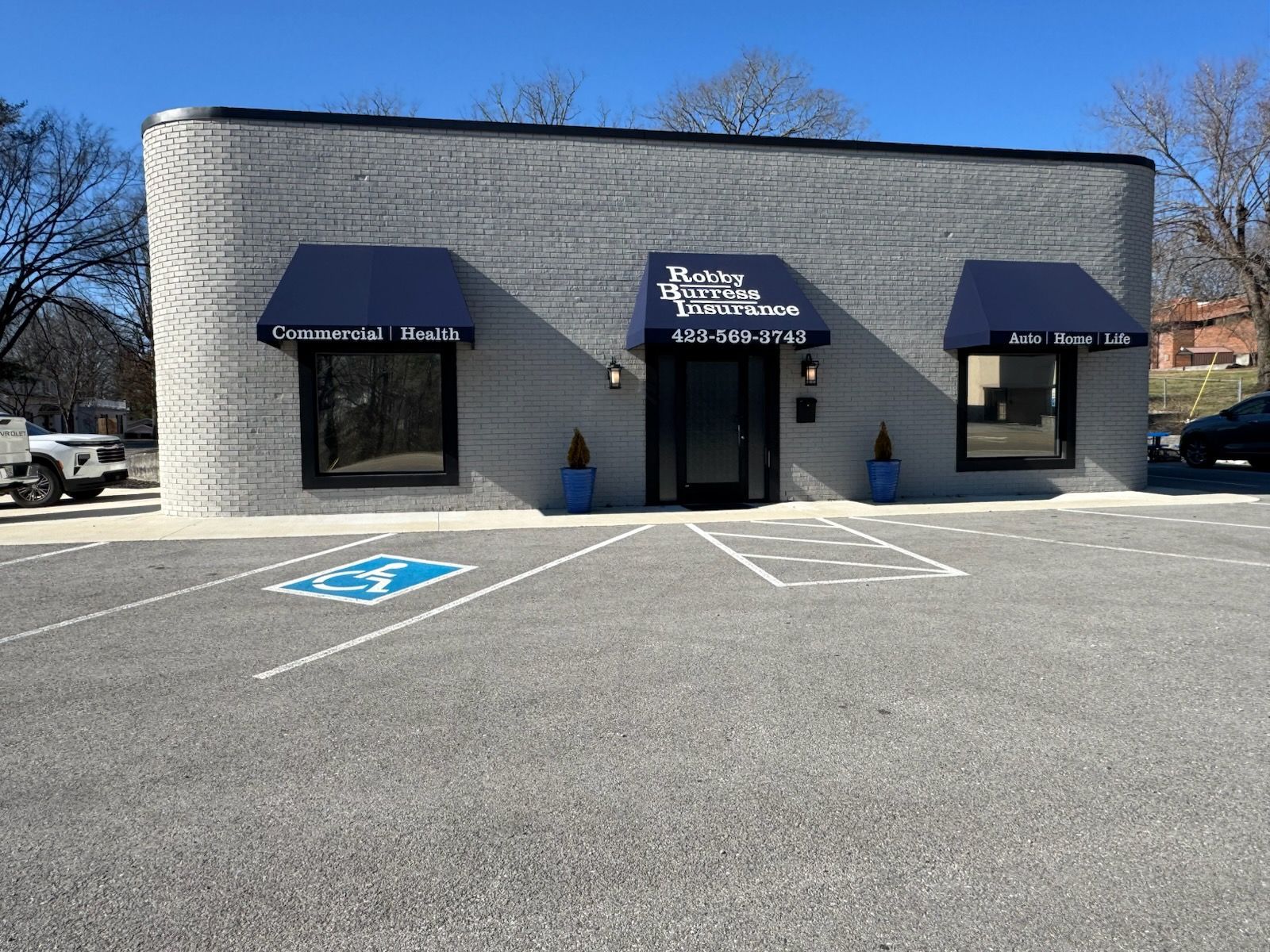 Small brick storefront with blue awnings and an accessible parking space in front