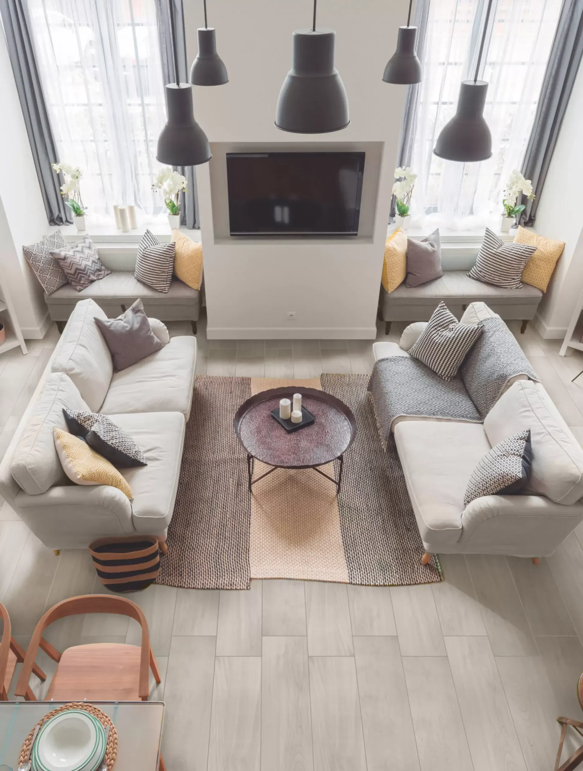 Una sala de estar simétrica con dos sofás claros, una alfombra estampada, una mesa de centro redonda y ventanas con asientos incorporados.