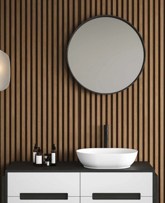 Un tocador de baño moderno con un lavabo blanco, un grifo negro y un espejo redondo contra una pared de listones de madera verticales.