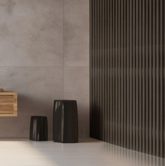 Interior minimalista con grandes azulejos de pared de color gris claro, una pared con acento oscuro acanalado y dos taburetes esculturales oscuros.