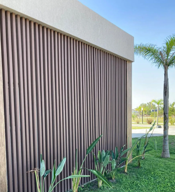 Una puerta moderna oscura con listones de madera verticales, un porche de hormigón y un alero de metal negro debajo de una estructura de hormigón.