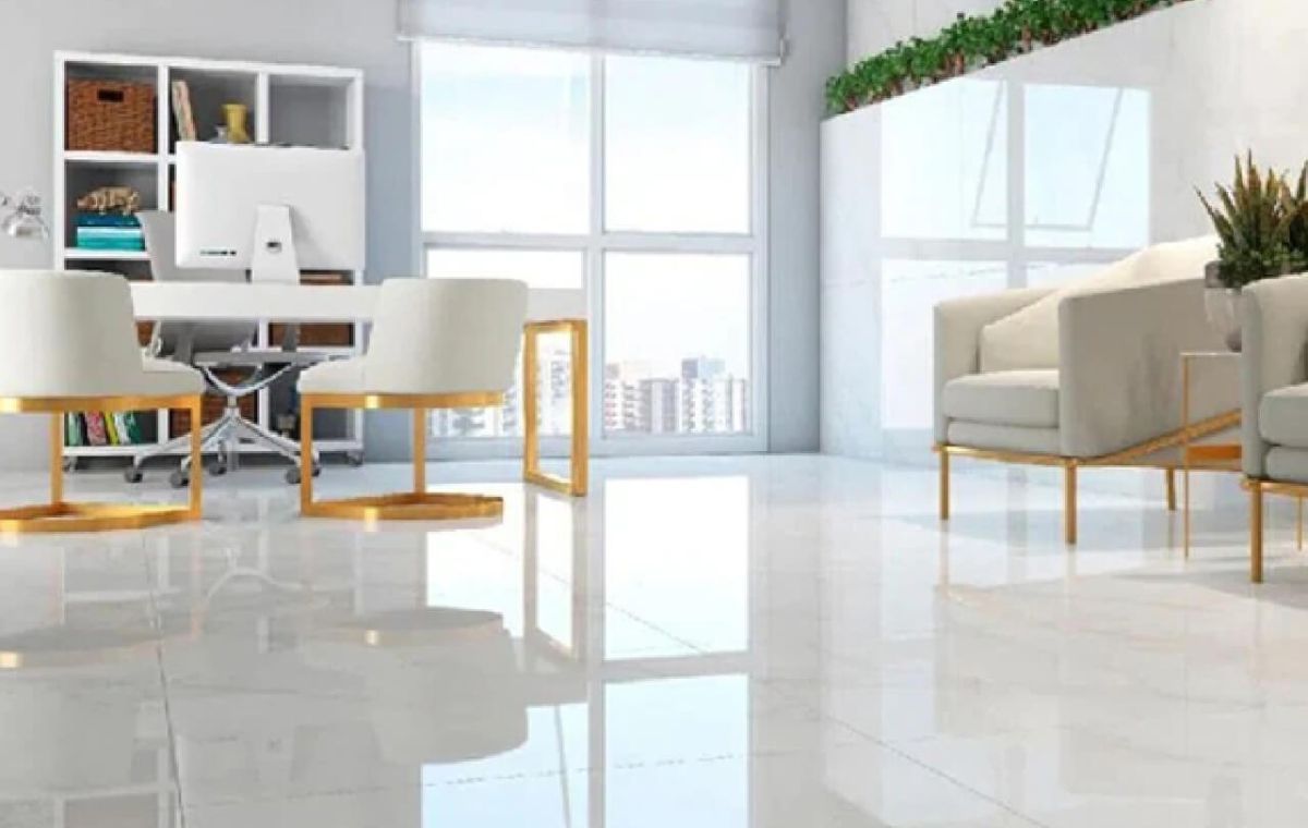 Una oficina luminosa y moderna con un escritorio, sillas blancas, estantería y una zona de estar con suelo de baldosas blancas y grandes ventanales.