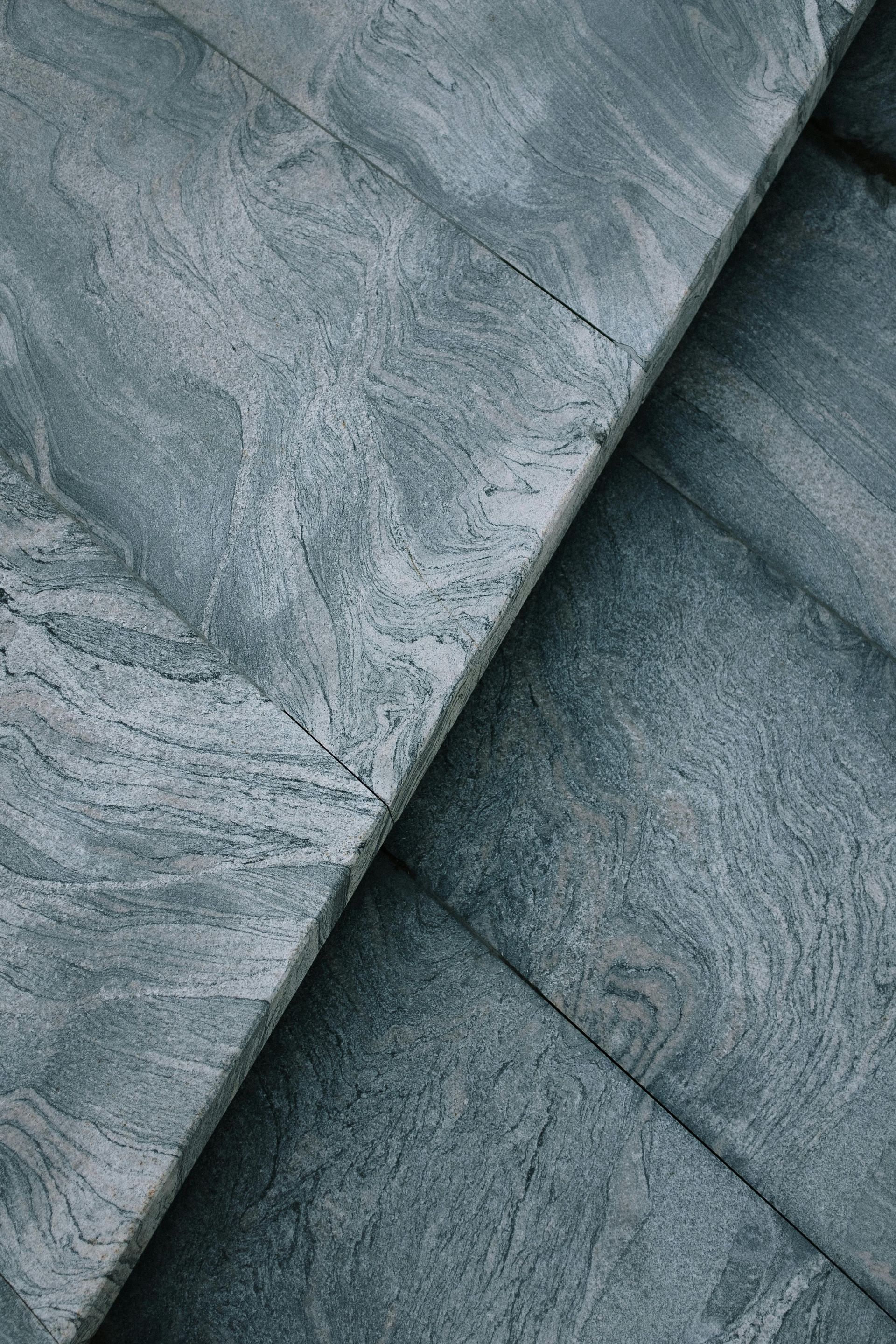 Primer plano de losas de piedra gris superpuestas con patrones texturizados y remolinos y bordes diagonales limpios.