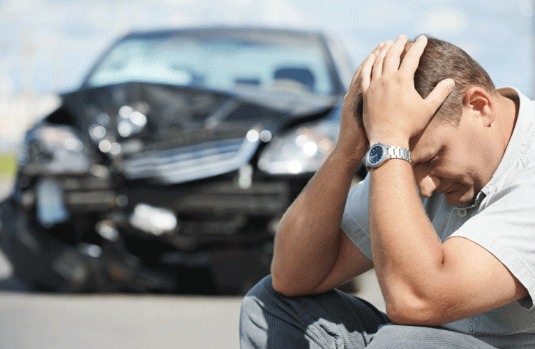 A man is kneeling down in front of a damaged car.