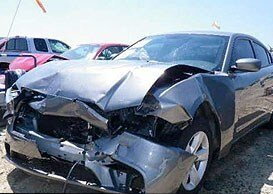 A gray car with a damaged front end is parked in a lot.