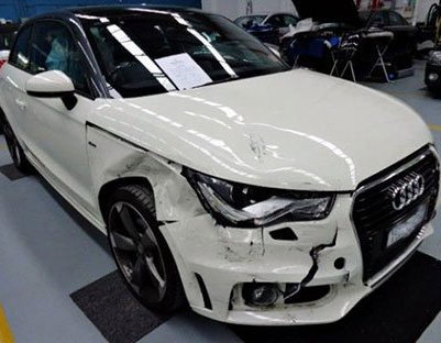 A white audi a1 is sitting in a garage with a damaged front end.