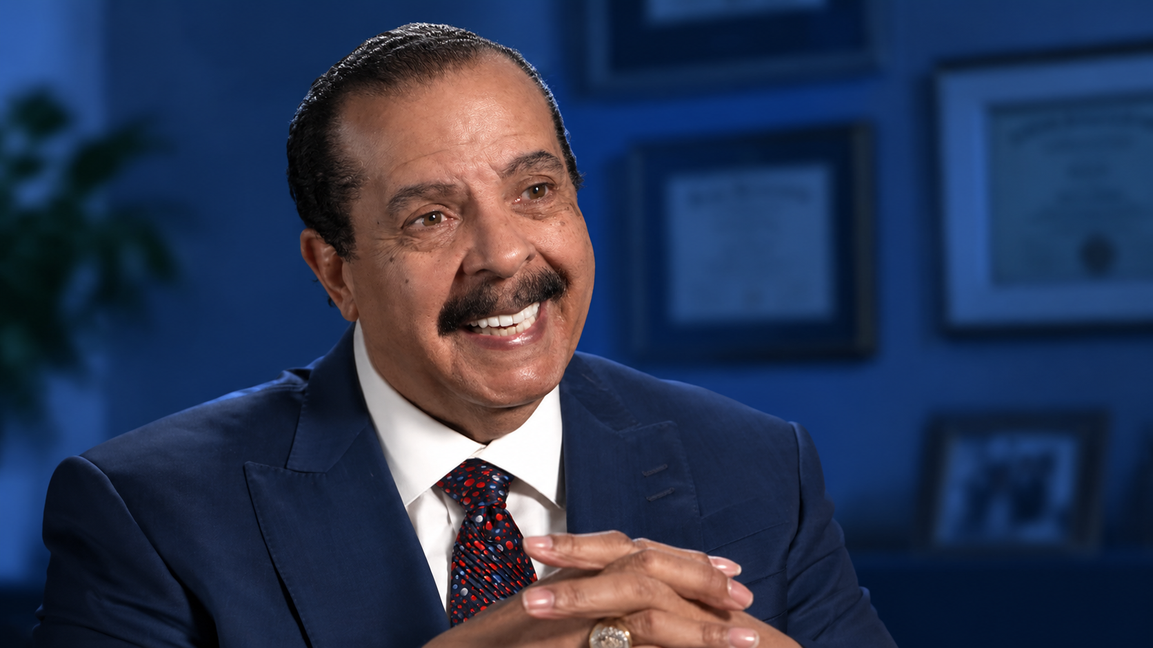 Smiling man in a navy suit speaking in a blue-toned office setting