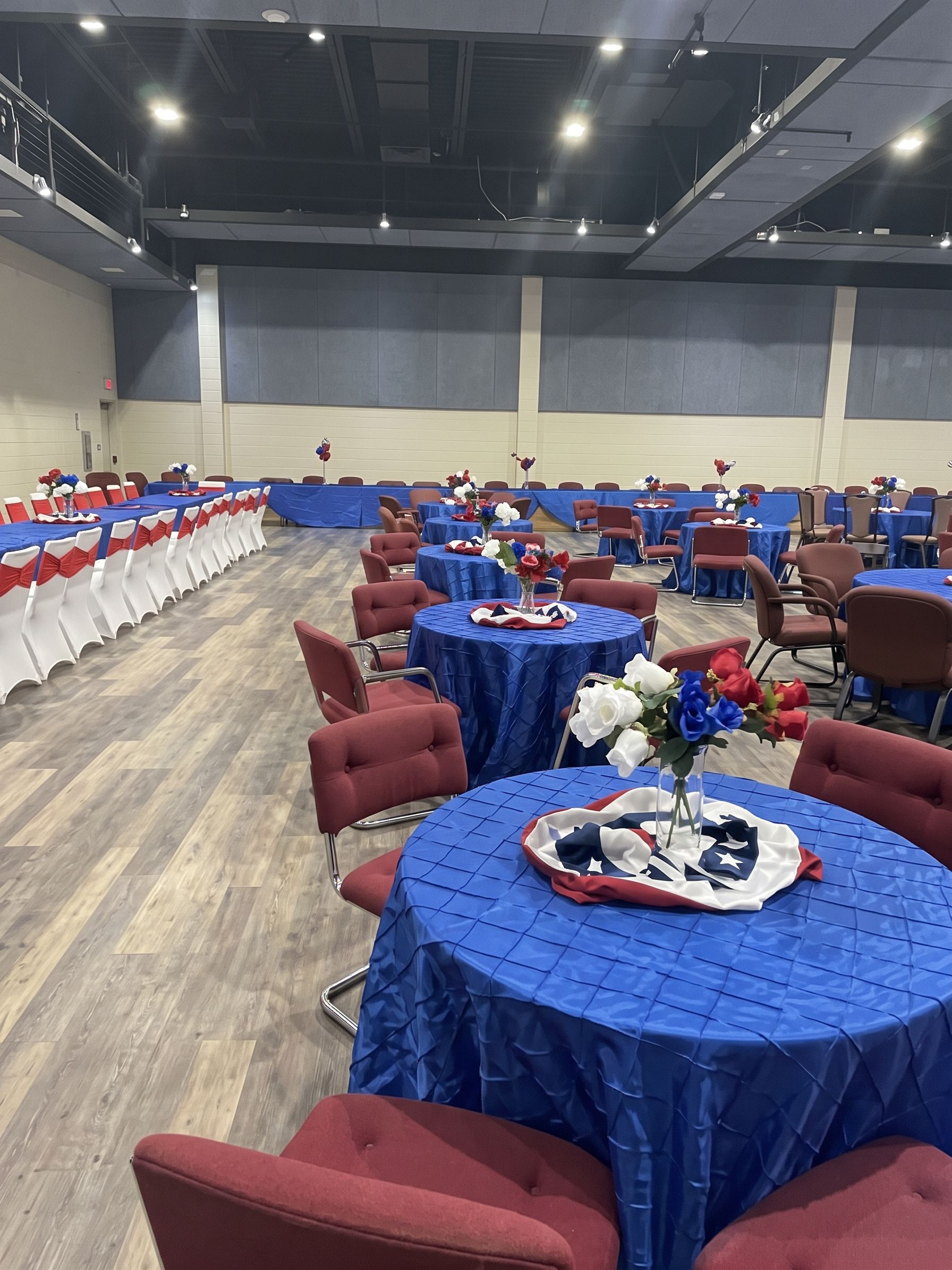 Elegant banquet hall with round tables, white chairs, floral centerpieces, and a large presentation screen