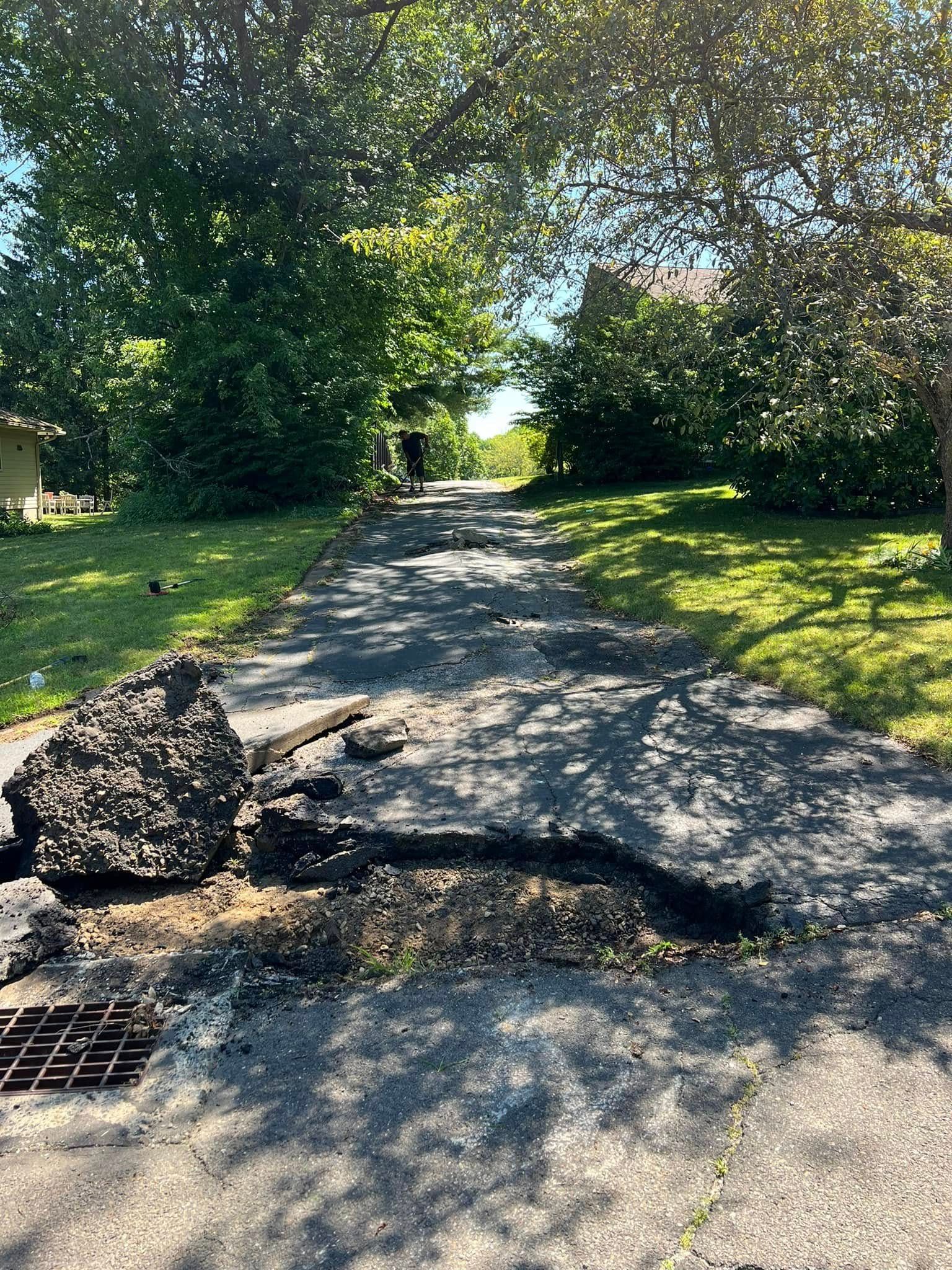 Sunlit cracked asphalt path with potholes and broken debris in a leafy residential area