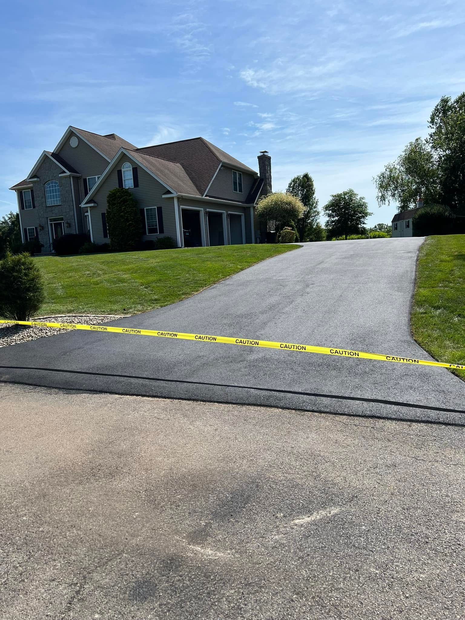 Yellow caution tape blocks a driveway leading to a large house on a sunny day