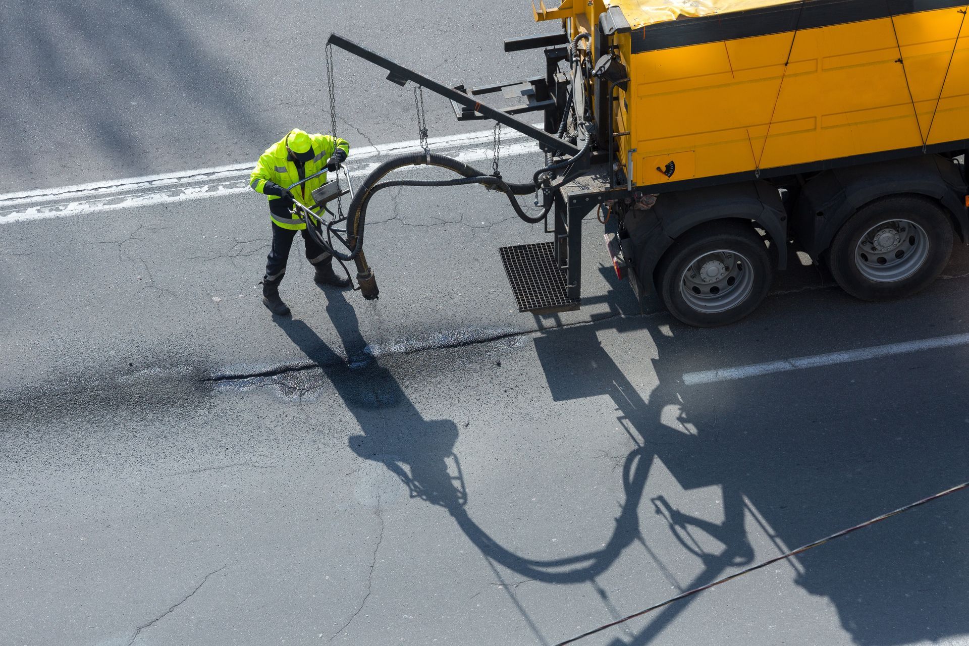 Worker in neon safety gear operating a road paver, laying asphalt on a street.