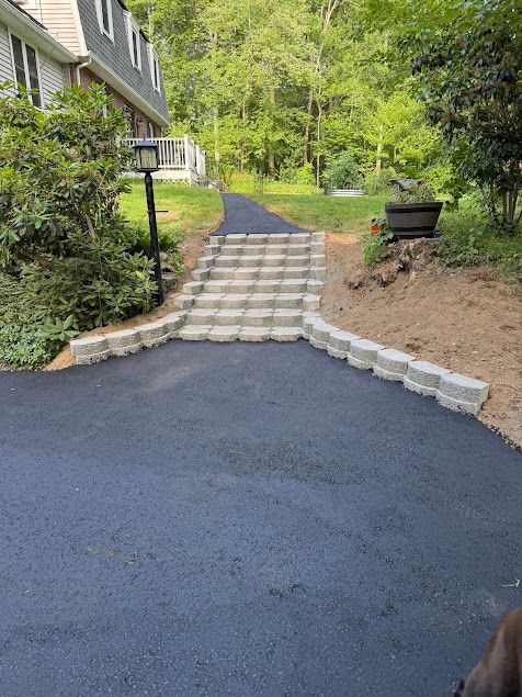 Stone steps lead from a driveway to a wooded yard beside a house.
