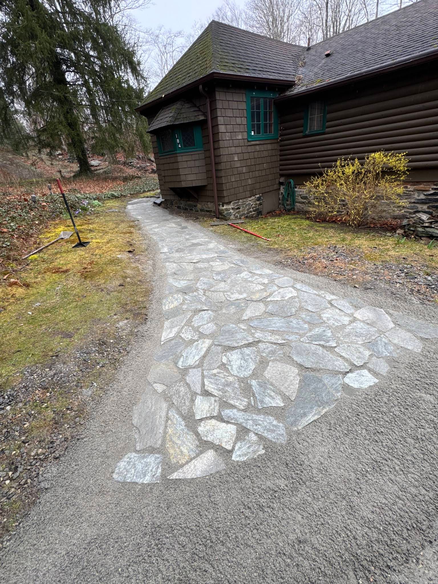 Stone path leading to a rustic wooden cabin with green-trimmed windows in a wooded yard