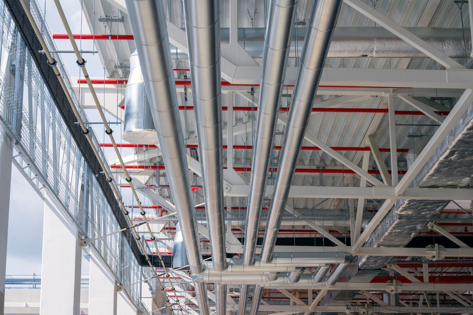 Interior of a modern industrial building with exposed steel beams, pipes, and large windows