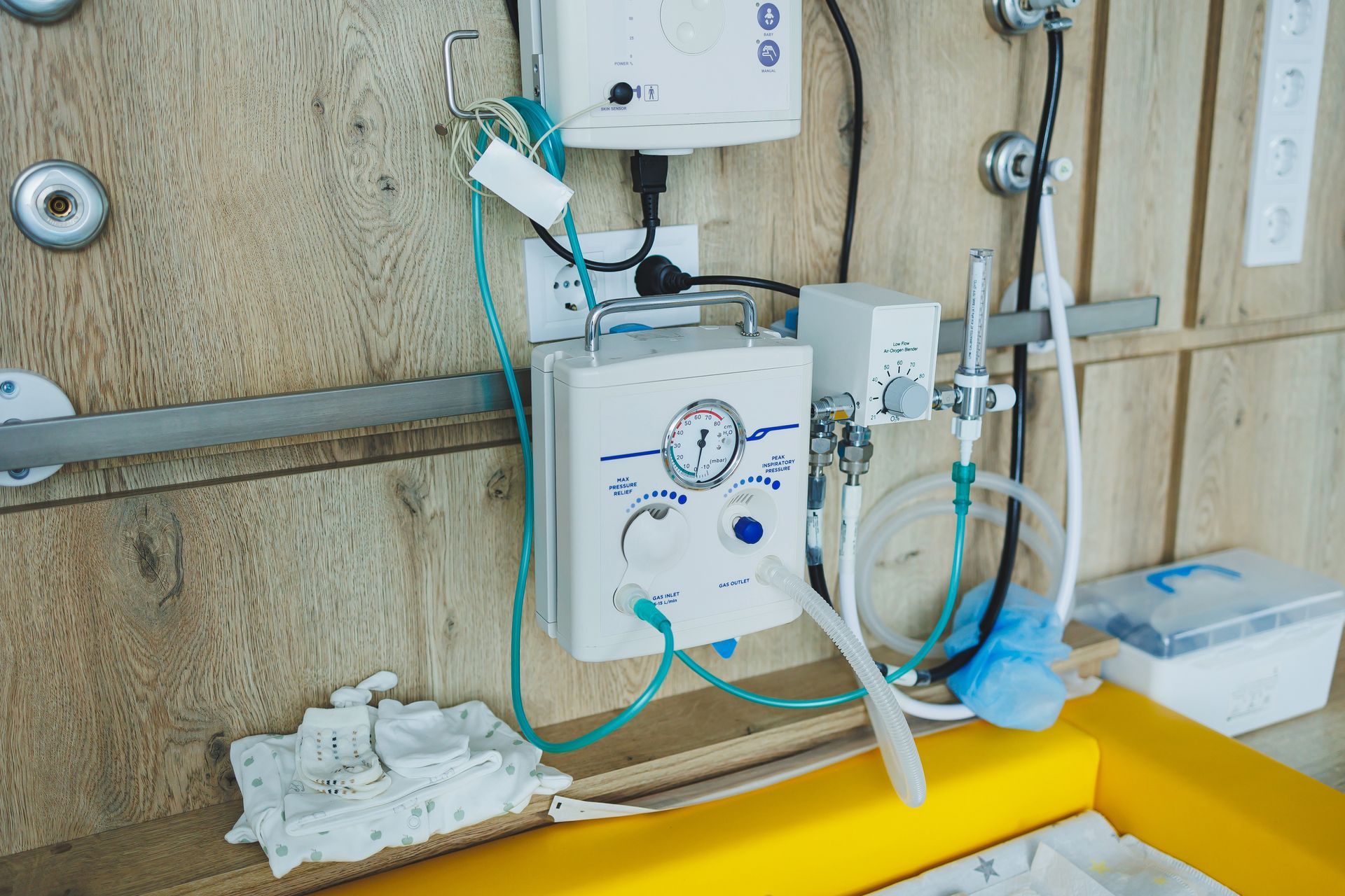 Industrial wall-mounted equipment with white and blue hoses on a plywood wall, above a yellow pipe