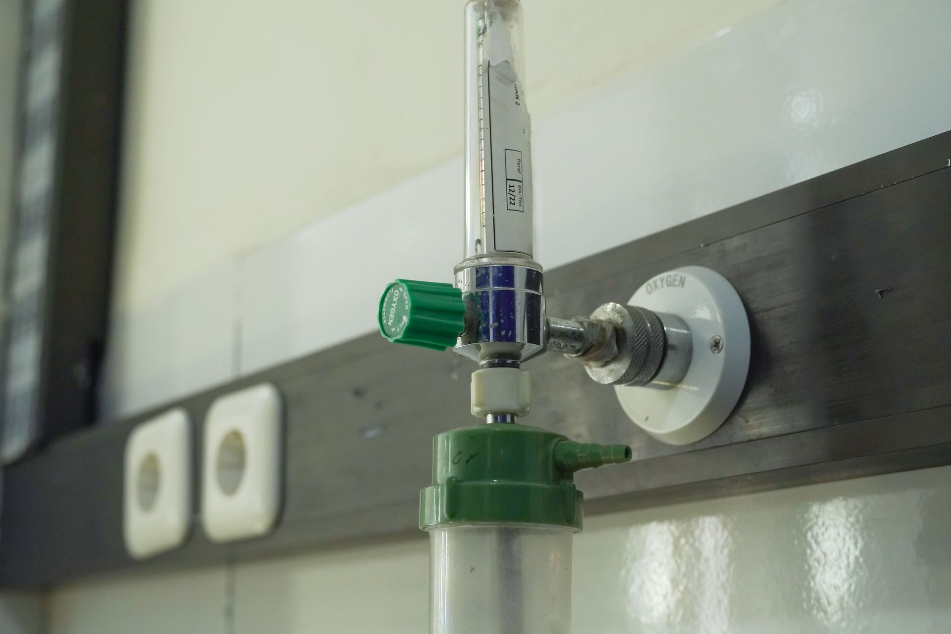 Close-up of a glass lab burette with green valve mounted on a tiled wall bracket