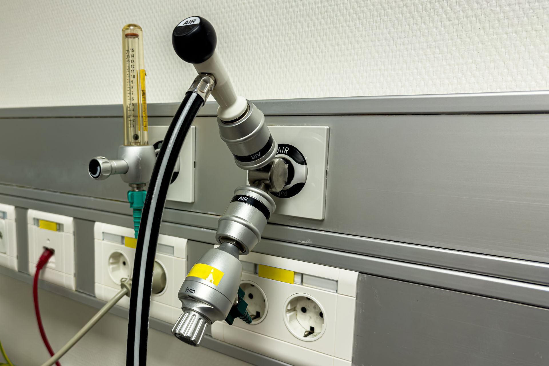 Lab gas outlet with connected tubing and valves mounted above wall power sockets.