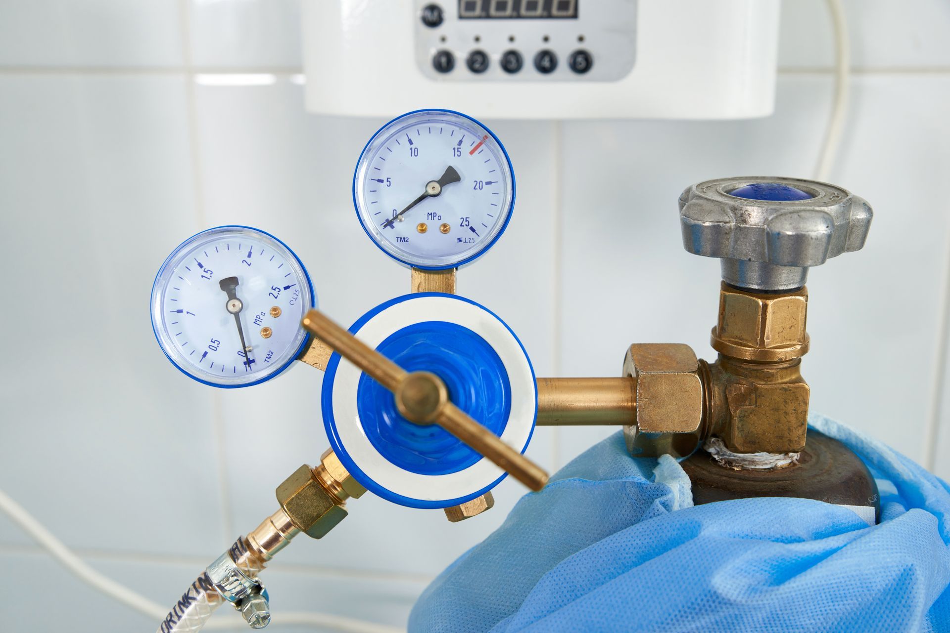 Blue gas regulator with two gauges and a metal valve being adjusted by a gloved hand