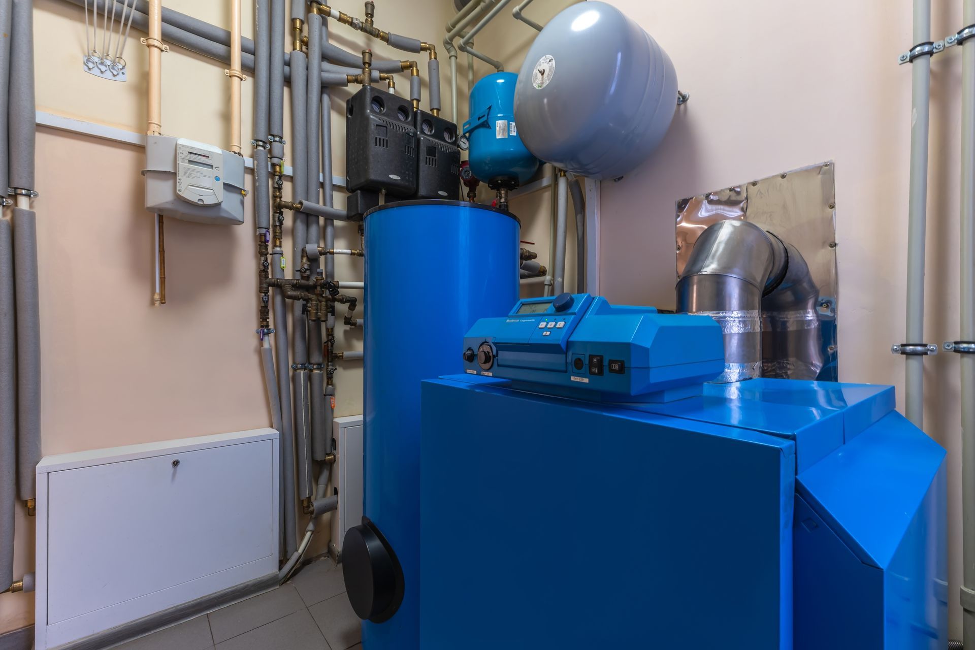 Blue industrial boiler and piping equipment in a utility room with a large silver ventilation duct.