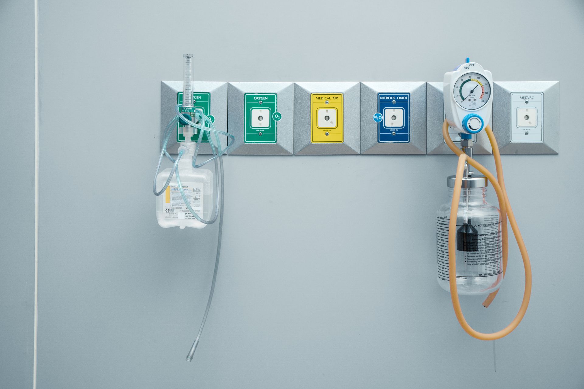 Hospital wall with oxygen, suction, and electrical outlets, plus hanging IV and medical tubing.