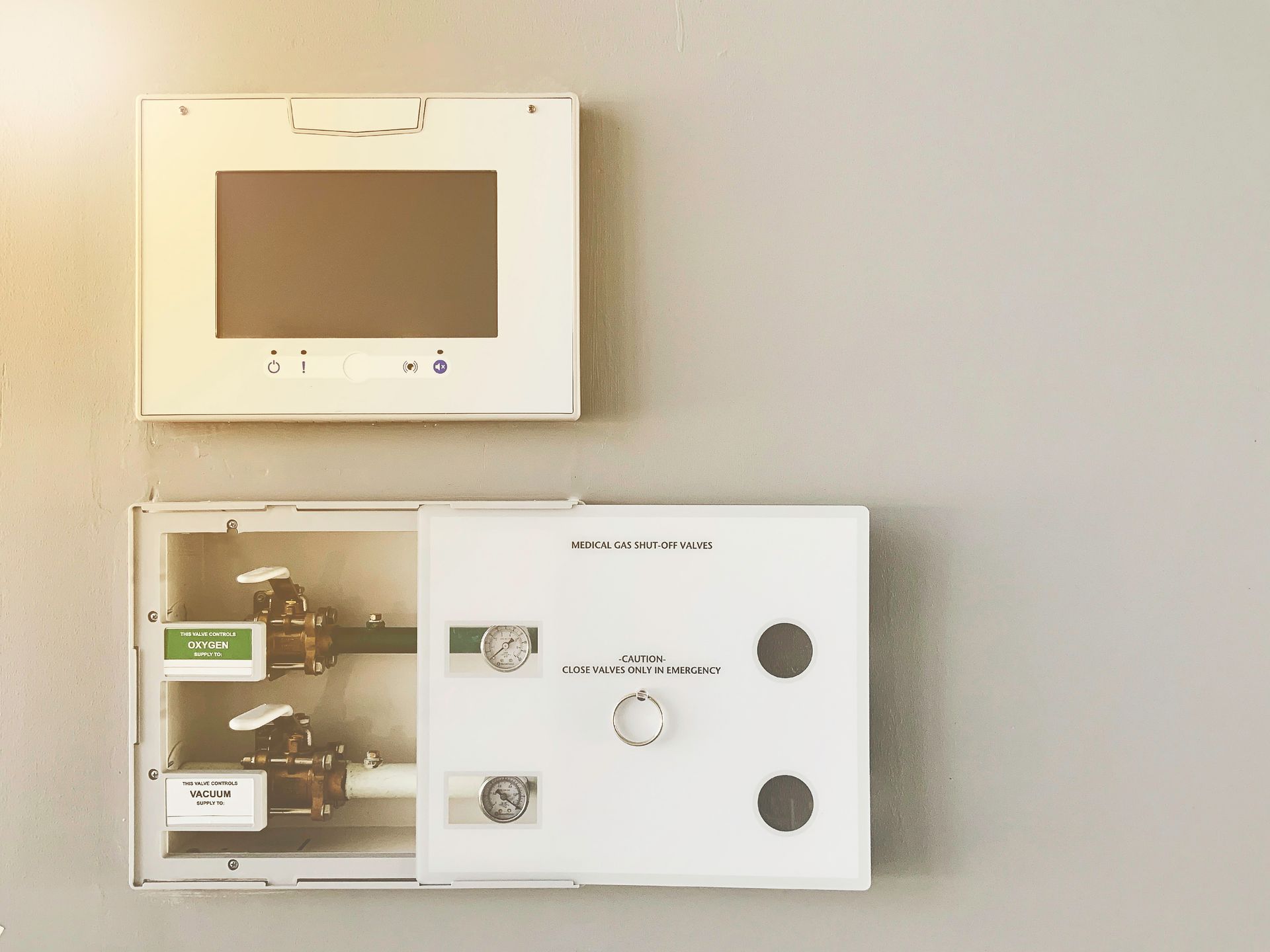 Wall-mounted thermostat and control panel on a beige wall, with a digital screen and buttons.