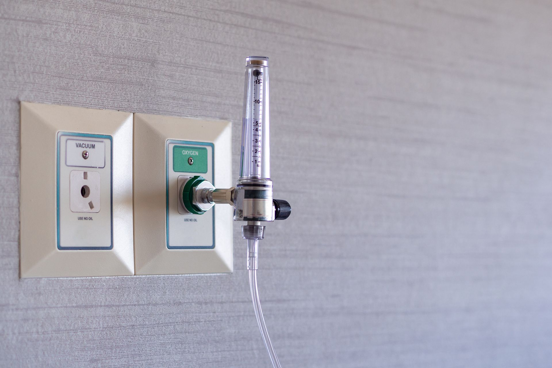 Wall-mounted oxygen flowmeter and outlet on a hospital wall with a clear tube attached.