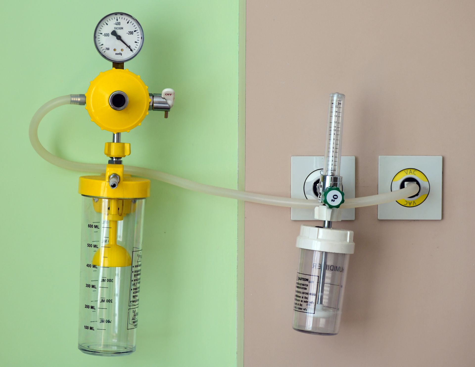 Two medical gas regulators with clear tubing, one yellow and one silver, mounted on a wall
