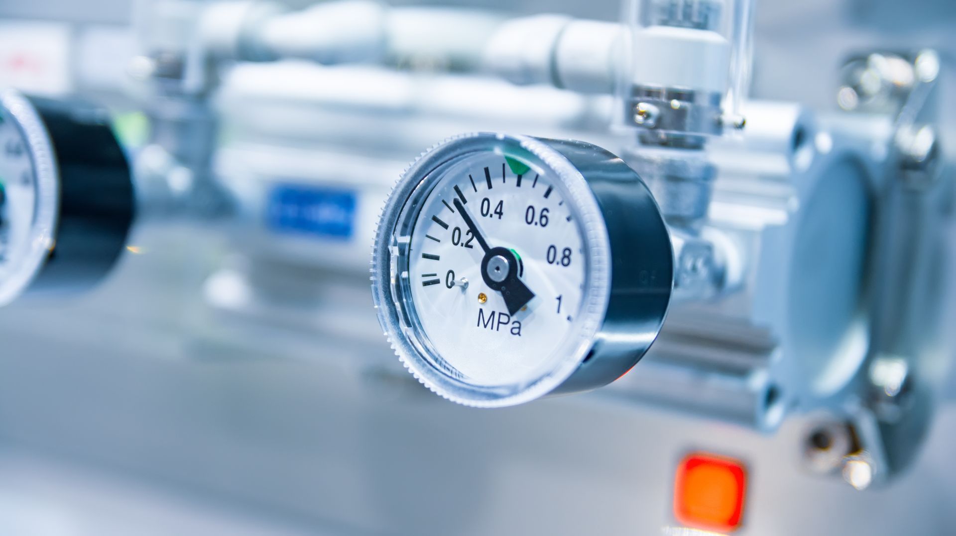 Close-up of a pressure gauge on industrial equipment, with a blue-toned metal background.