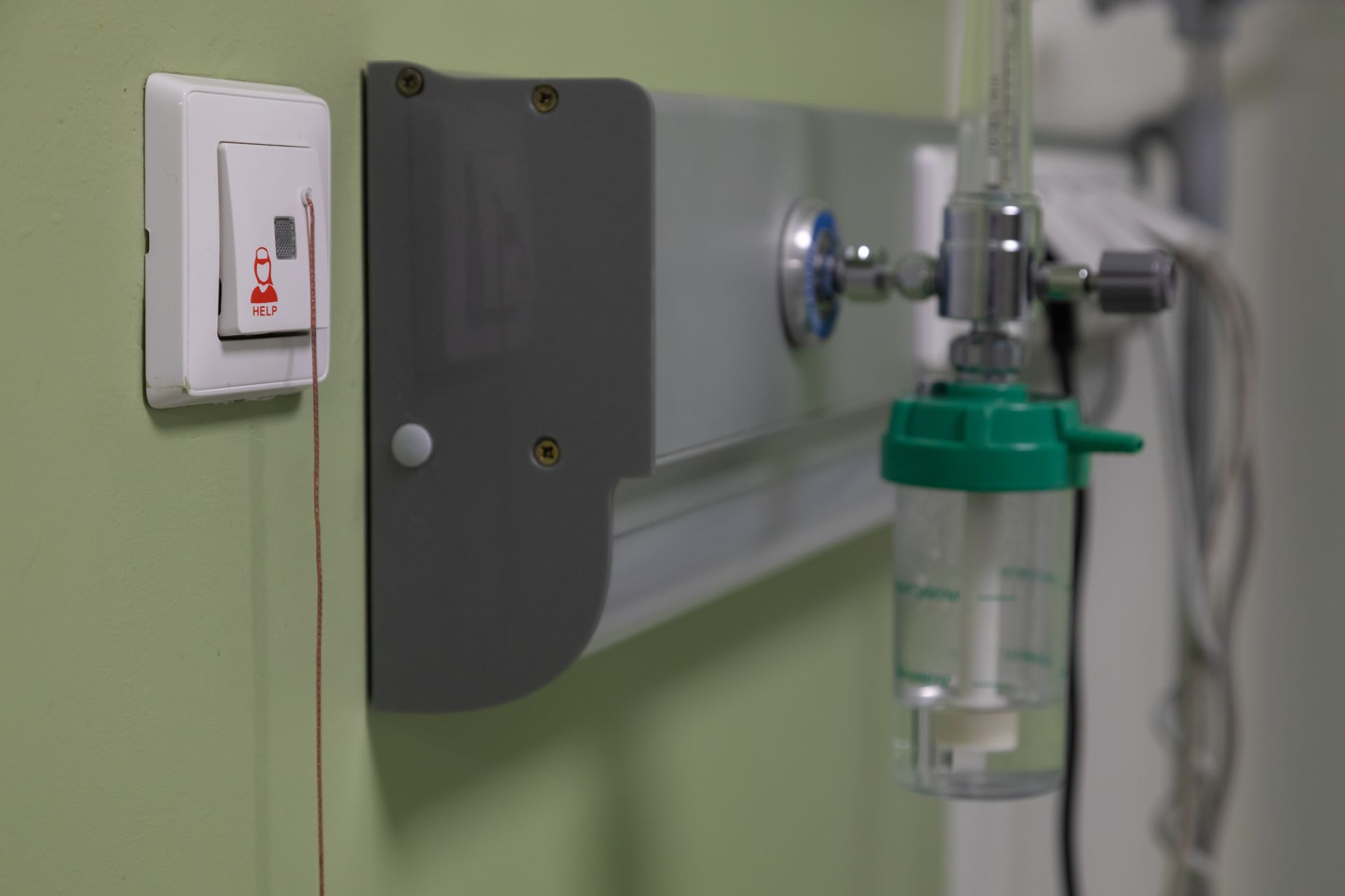 Hospital wall with oxygen and suction outlets, a green oxygen flowmeter, and a wall switch.