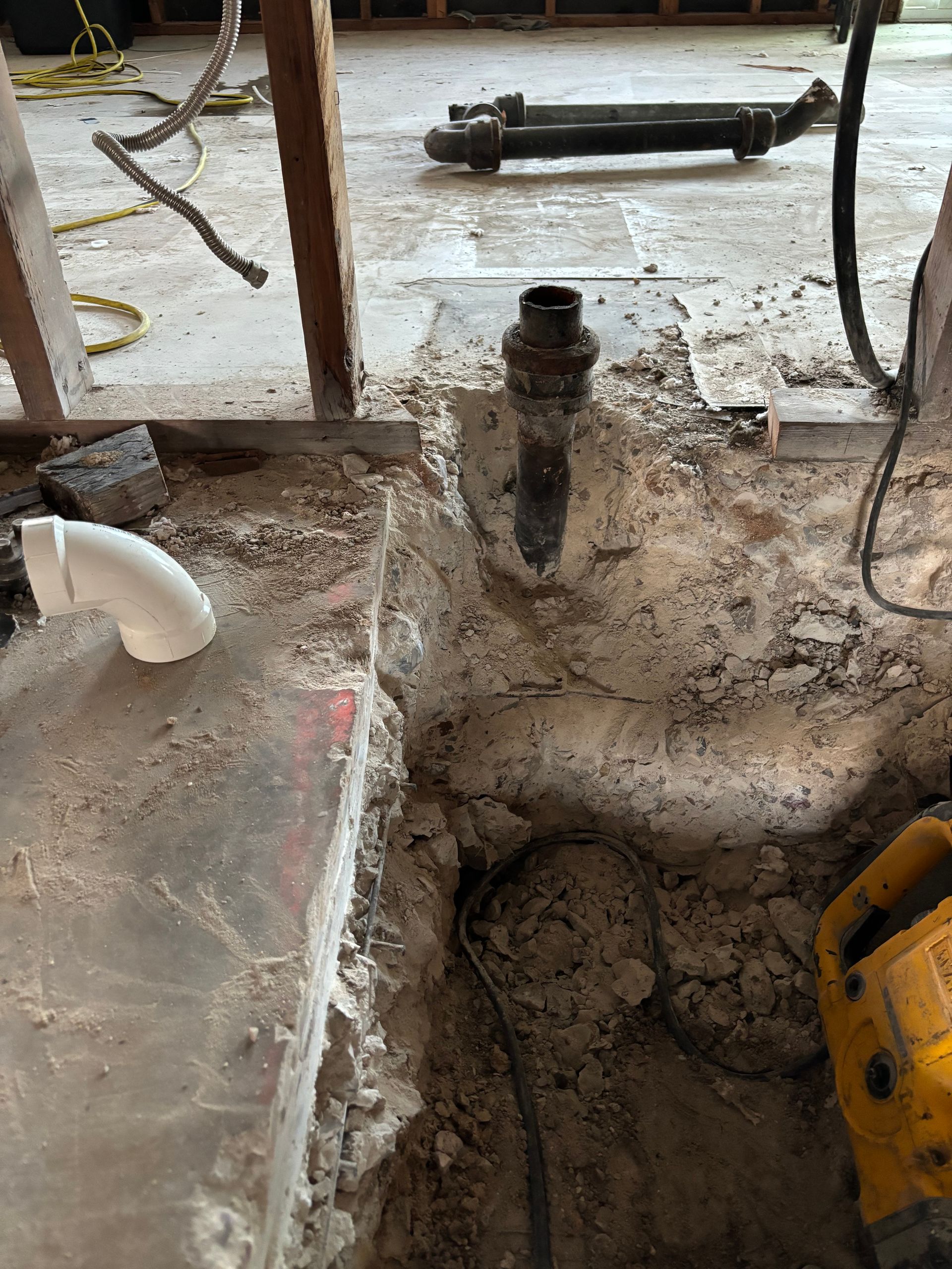Orange PVC pipe being installed in a dirt trench with workers' hands visible