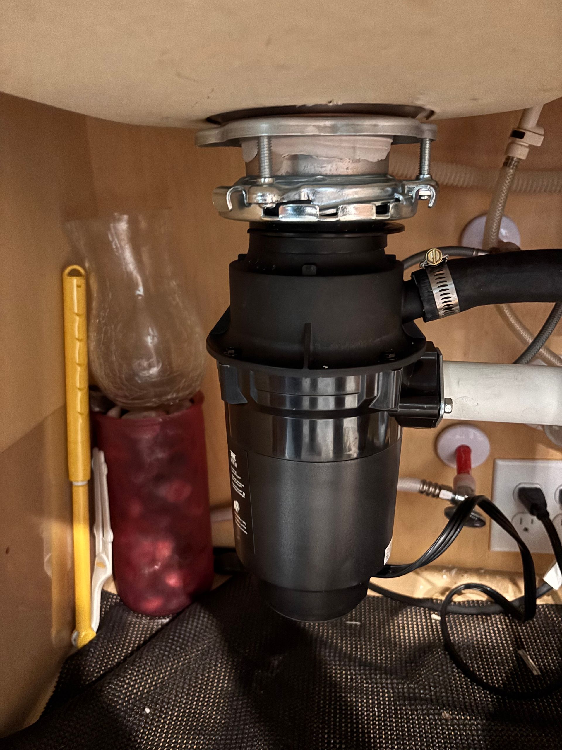 Person using a red pipe wrench to tighten plumbing under a sink