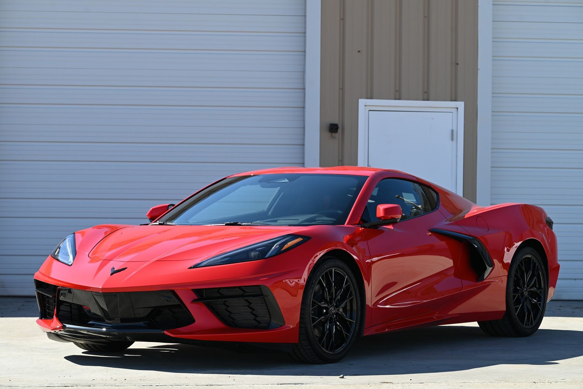 Red Chevrolet Corvette sports car parked in front of a building with a closed garage door.