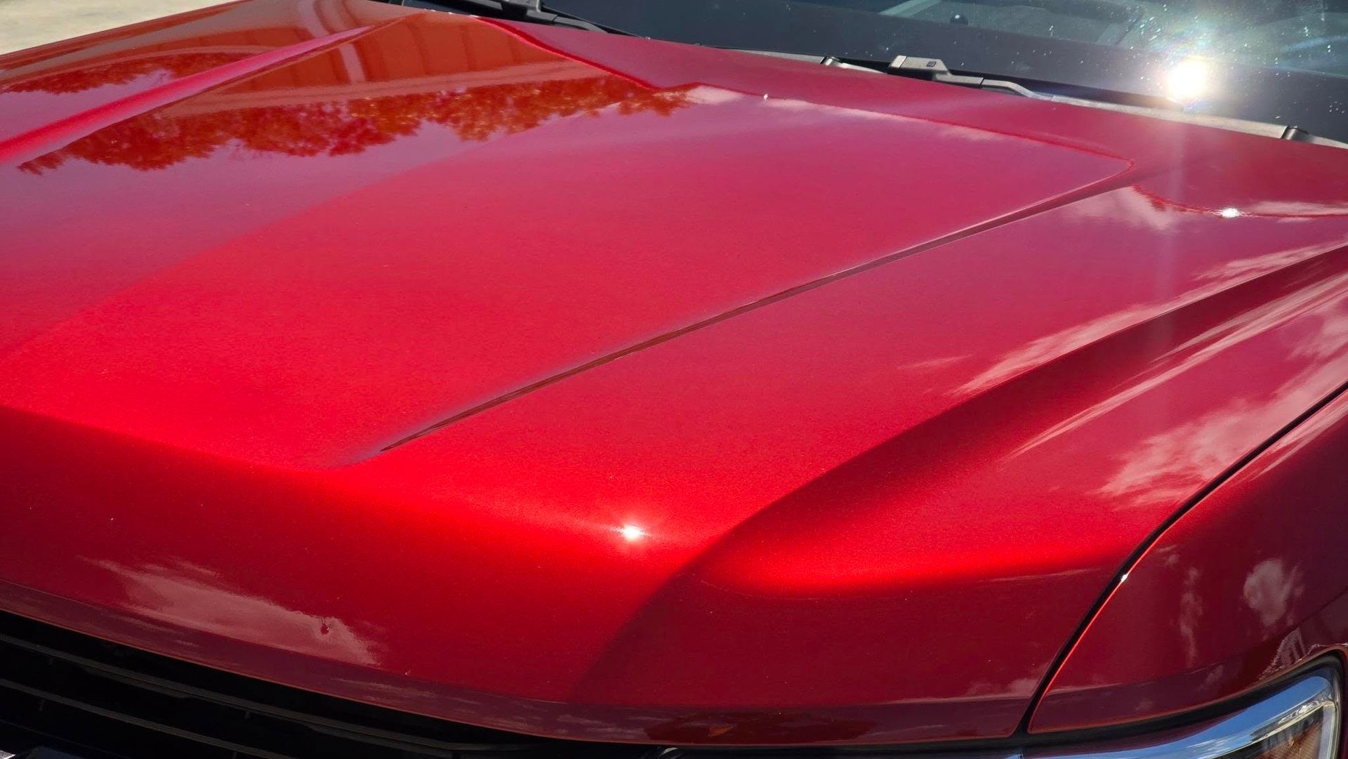 Red car hood, shiny with sunlight reflection, showing paint texture.