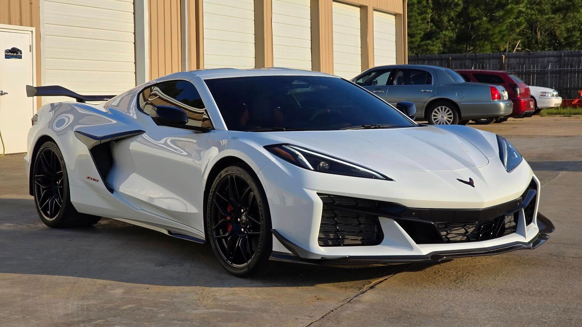 White sports car parked in front of a building; other cars in the background.