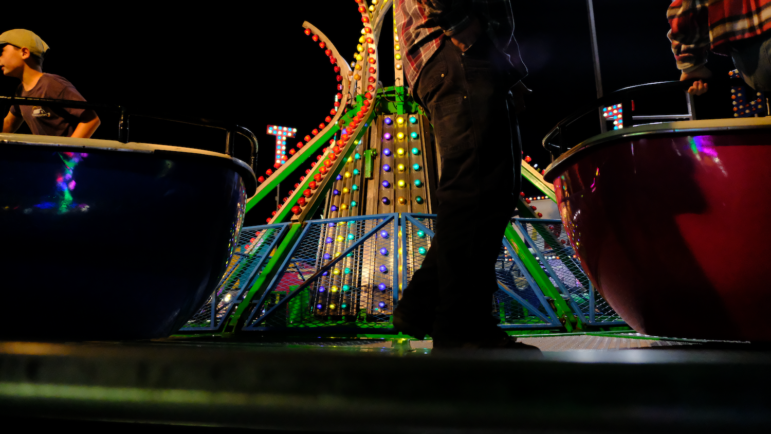 Carnival ride at night with colorful lights and people standing near spinning pods.