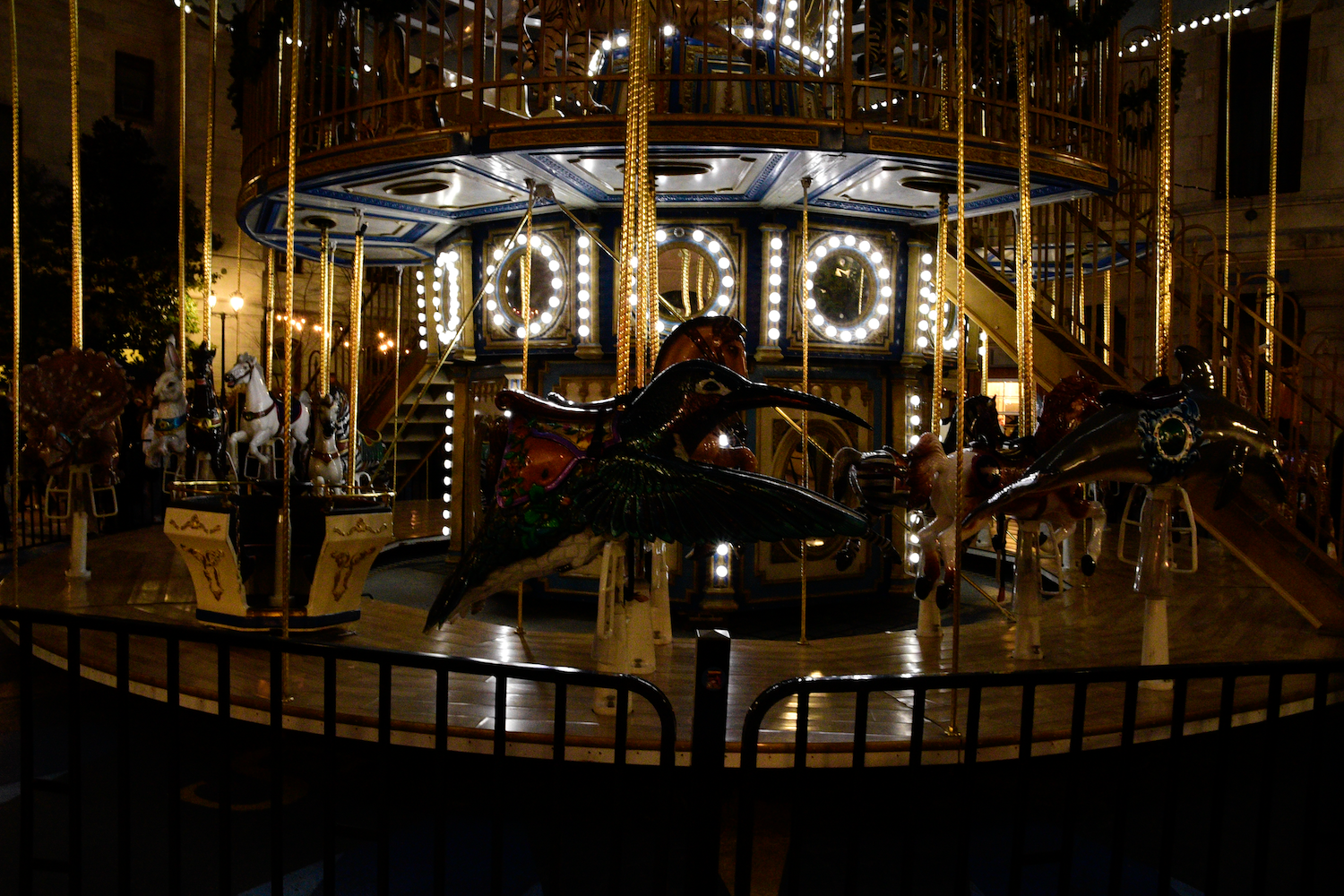 Lit-up carousel at night. Features animal figures, lights, and railings.